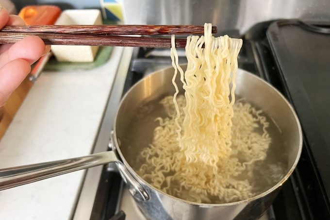 holding Ramen with chopsticks, removing it from a pot of water on the stove