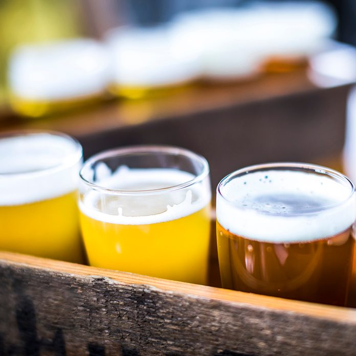 Flight of four beers lined up on a wooden table, with selective focus. Photo taken outdoors with natural lighting; beers range in color from light to very dark. Background out of focus.