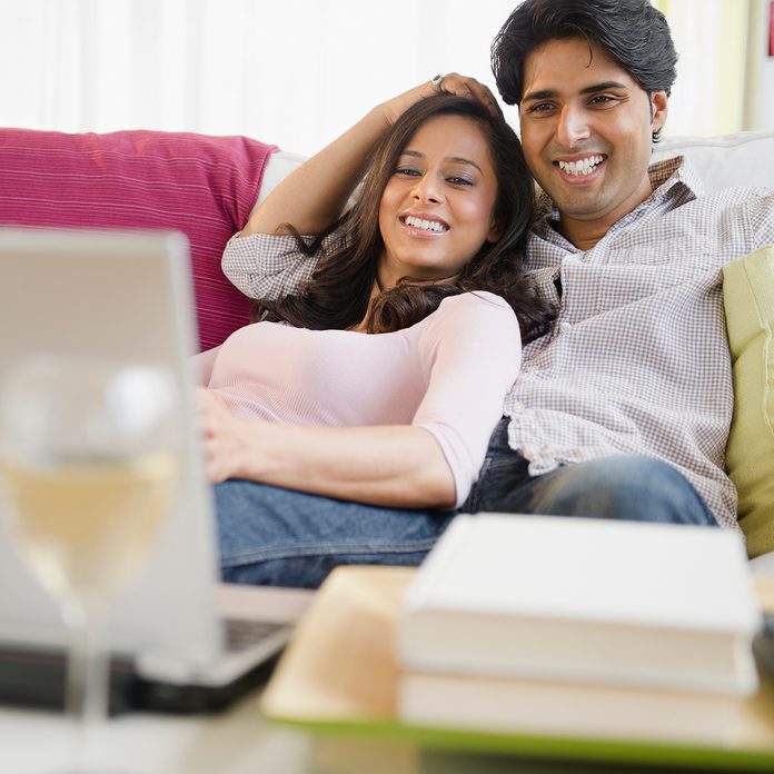 Happy Mixed Race Couple Relax On Couch In Living Room Watch Movie