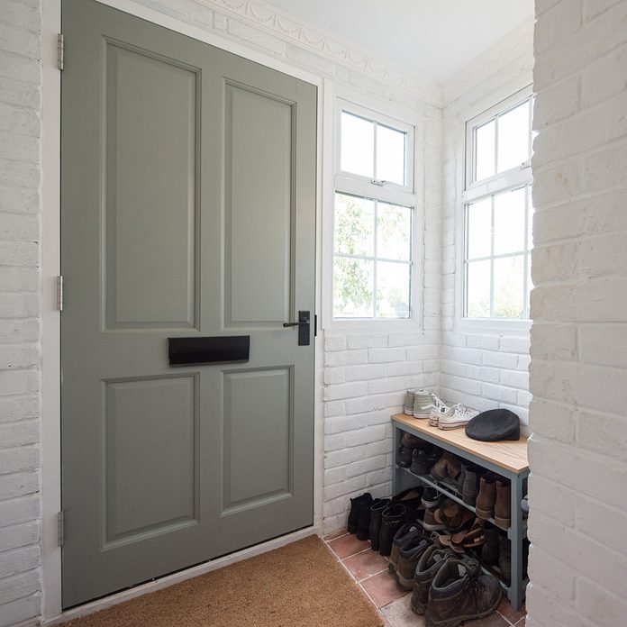 A general interior view of a entrance hall porch with sage green front door and shoe rack storage within a home