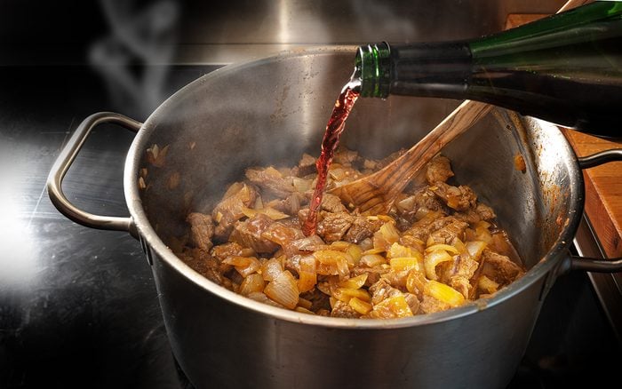 cooking wine Red Wine Is Poured From A Bottle Into A Pot With Roasting Goulash To Deglaze, Cooking At Home Concept, Selected Focus