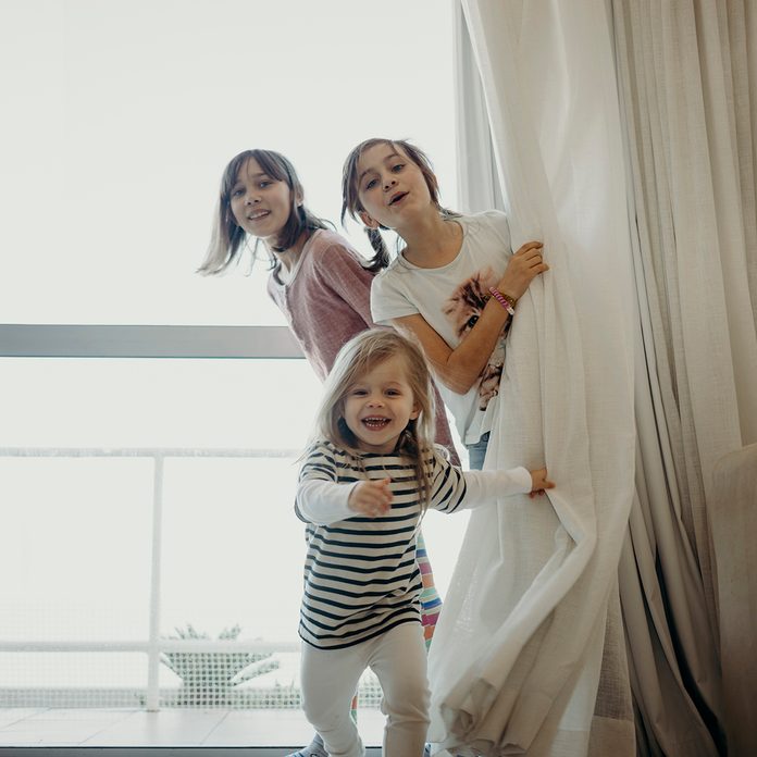 Three Young Girls Peer From Behind Curtain