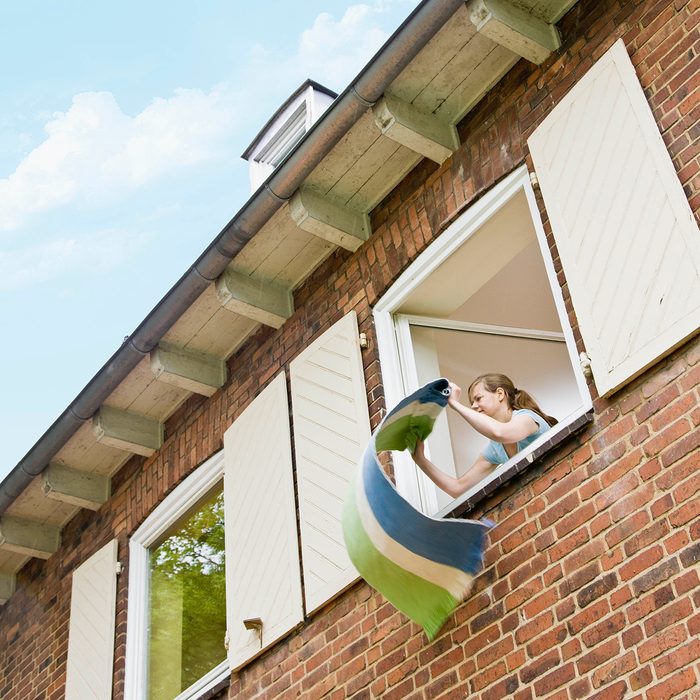 Woman Cleaning A Rug Out A Window