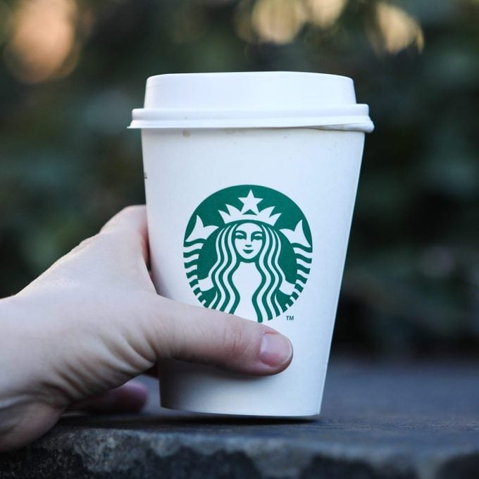 hand holding a disposable coffee cup with a starbucks logo outdoors at twilight