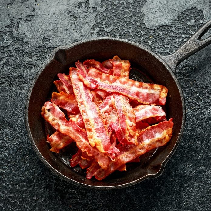 Fried crunchy Streaky Bacon pieces in a cast iron skillet.