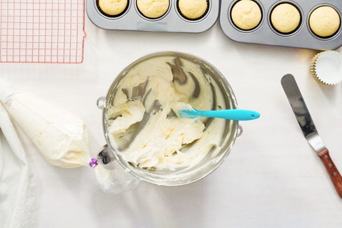 frosting in a stand mixer mixing bowl ready to be scooped into a piping bag for cupcakes nearby