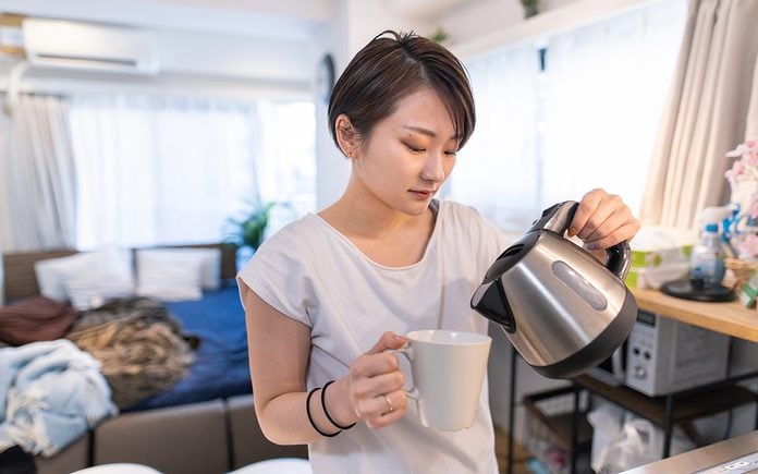 electric tea kettle review Young Woman Pouring Coffee For Breakfast