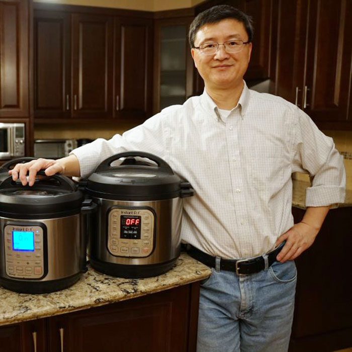 Robert Wang standing next to two models of instant pots in a kitchen