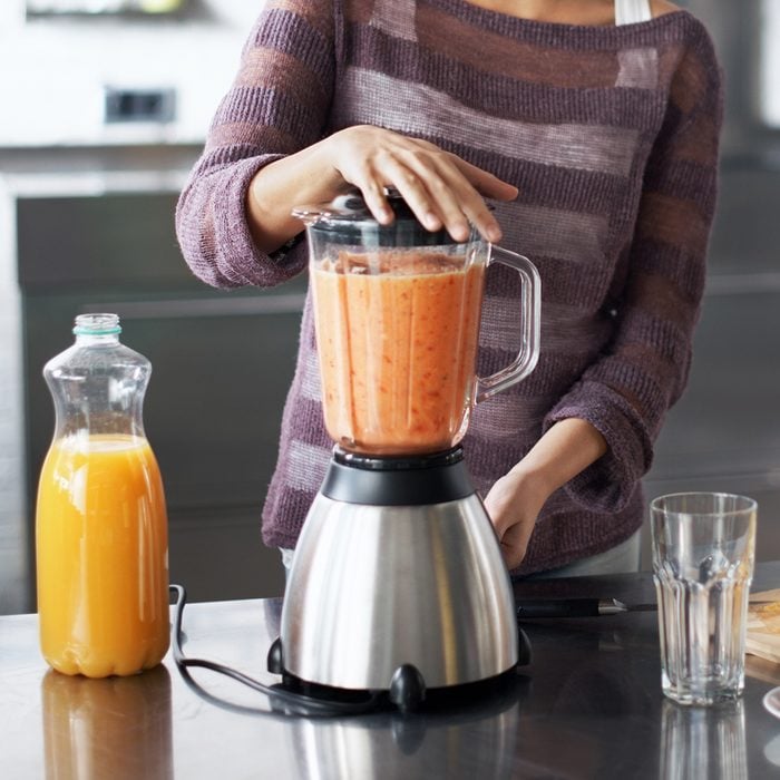 how to make frozen drinks A woman smiling happily while preparing a smoothie in her kitchen at home