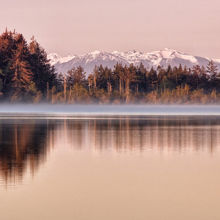 Dawn at Cranberry Lake in Deception Pass State Park in Washington State. Trees are reflected in the lake and the Olympics (Olympic Mountains) are visible in the distance.