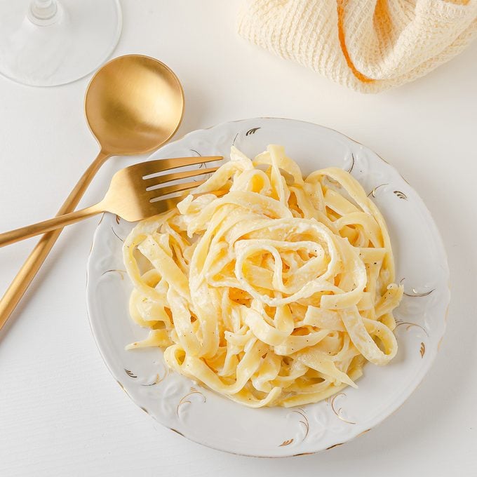 Traditional Italian Pasta Fetuccini Alfredo On A White Table With Golden Appliances