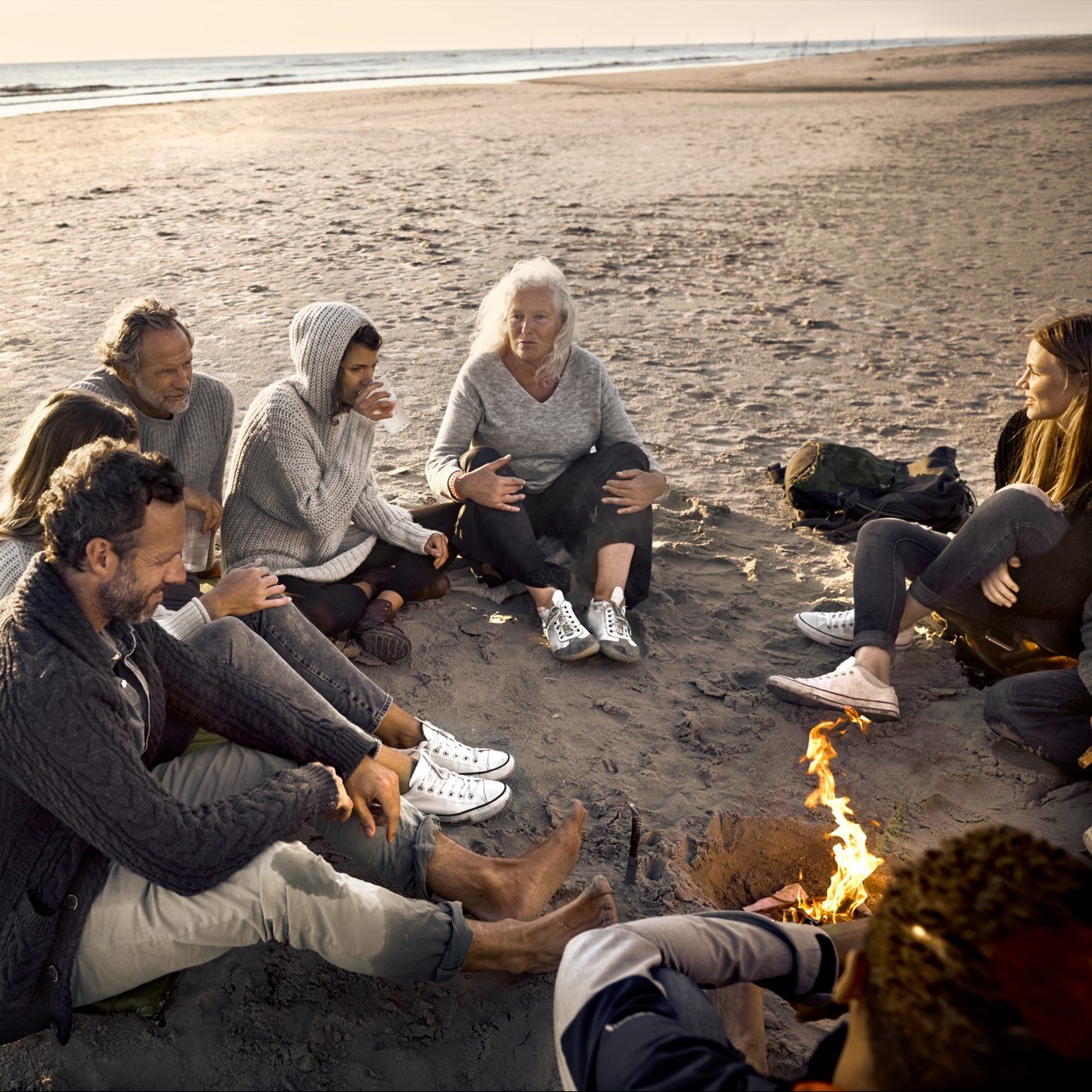 Family and friends sitting around campfire on the beach at sunset