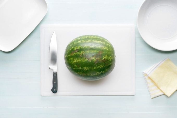 a whole watermelon on a white cutting board and a knife to the side