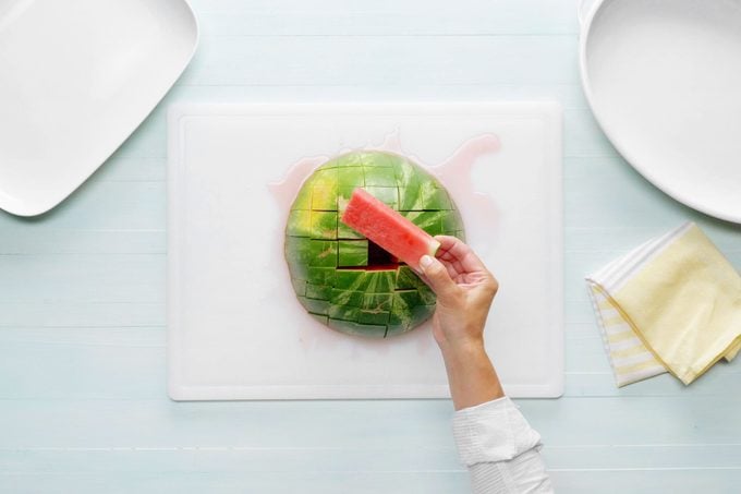 a hand removing a stick of watermelon from the center of the watermelon