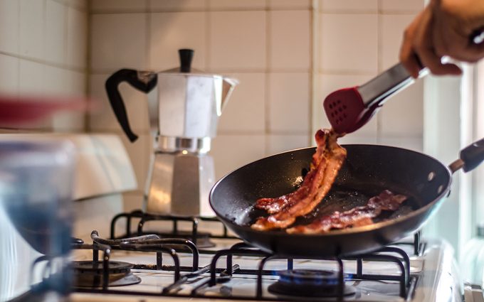 pancetta vs bacon Cropped Hand Cooking Bacon On Stove In Kitchen