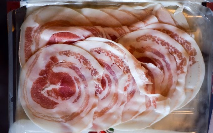 pancetta vs bacon Thin sliced pancetta bacon in an opened plastic pack. One of the ingredients in the preparation of "Coniglio al forno con pancetta e erbe aromatiche", roasted bacon-wrapped rabbit with aromatic herbs