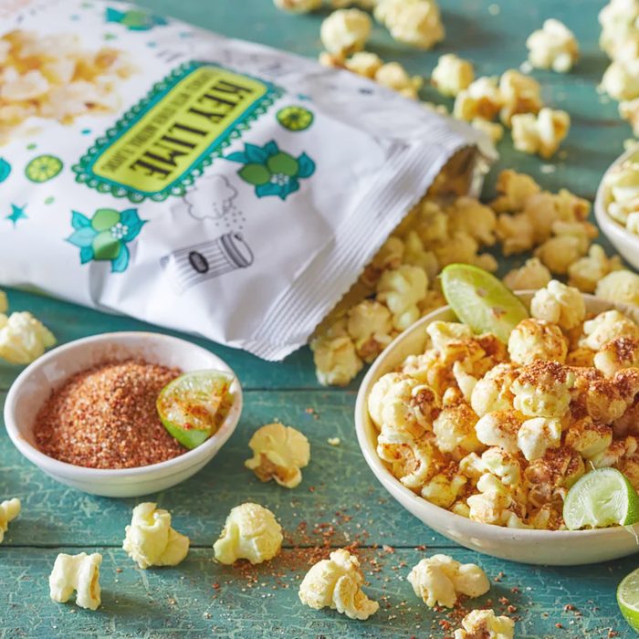 Trader Joe's Key Lime Popcorn in bowls and scattered on surface; one bowl sprinkled with chili lime seasoning