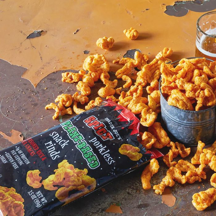 Trader Joe's Spicy Plant-Based Snack Rinds scattered on a vintage surface and in tin container; mug of beer in background