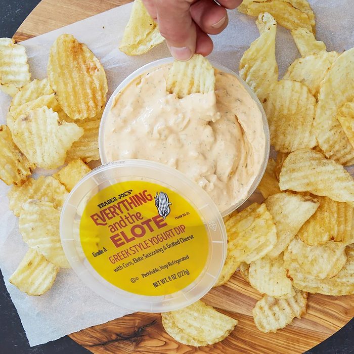 Trader Joe's Everything and the Elote Greek Style Yogurt Dip opened, with a chip being dipped, and surrounded by more chips