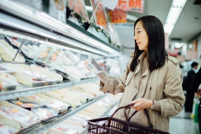 Young Asian woman grocery shopping and choosing fresh poultry in supermarket