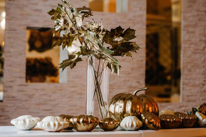 Golden pumpkin and dry bouquet leaves in vase on the table. Gold wedding reception. Luxury style elegant wedding decor for the ceremony. Autumn location and Halloween decor.