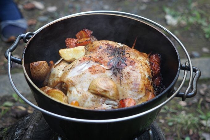 chicken cooking in dutch oven pot at campsite