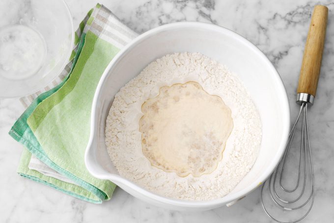 mixing dough for a pizza crust in a white plastic mixing bowl
