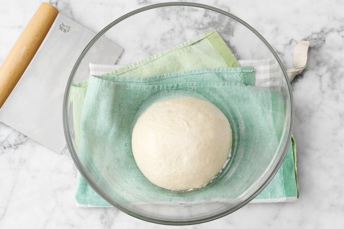 pizza dough resting in a clear class bowl so it can rise