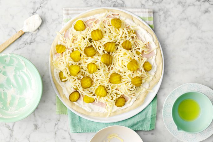 pizza dough topped with pickles before baking