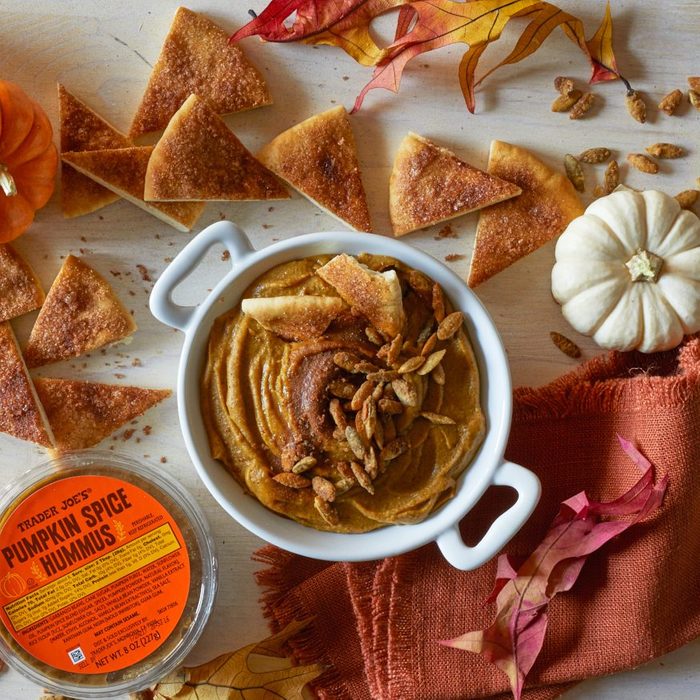 Trader Joe's Pumpkin Spice Hummus in a crock, sprinkled with pumpkin spiced pumpkin seeds and cinnamon and sugar. Pita bread wedges coated with cinnamon sugar and fall decorations surrounding