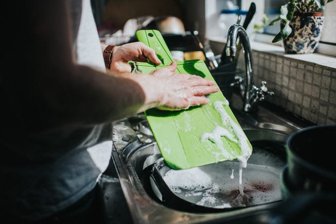 man washing a green plastic cutting board in the sink