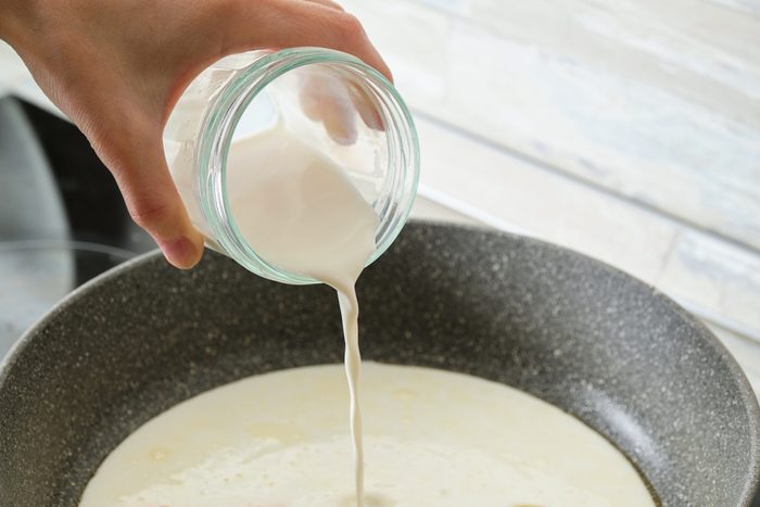 pouring heavy cream into skillet over the stove at home