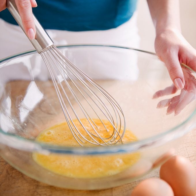 woman whisking eggs in large glass bowl