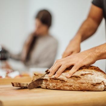 Young man slicing bread on cutting board in kitchen