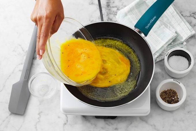 pouring eggs into skillet for scrambled eggs