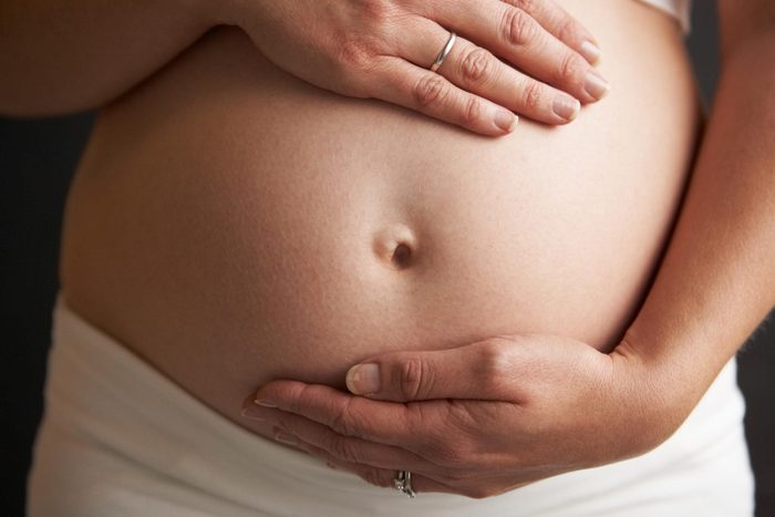close up pregnant belly with womans hands touching above and below