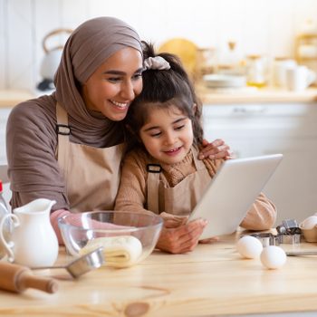 Islamic Lady Baking With Her Little Daughter In Kitchen, Using Digital Tablet
