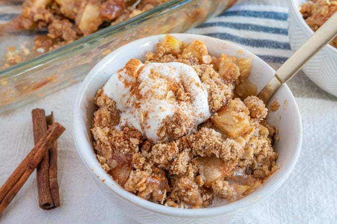 pioneer woman apple crisp served in a white bowl with ice cream