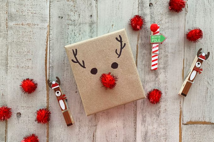 cristmas gift wrapped with brown paper and made to look like rudolf the red nosed reindeer with a red pom pom and drawn eyes and antlers