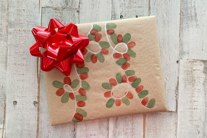 christmas gift wrapped in brown paper that has been decorated with thumbprint string of lights design