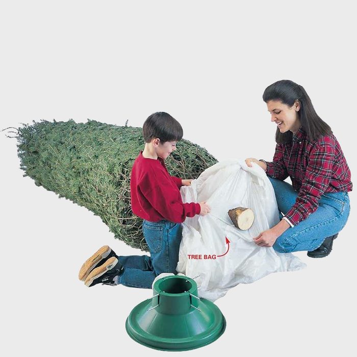 woman and boy placing a tree bag at the base of a christmas tree before standing it up in the stand