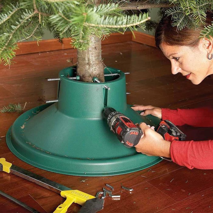 a woman tightens the bolts on a christmas tree stand using a drill