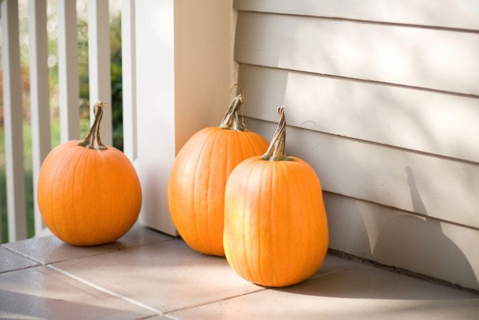 Three pumpkins sit on the porch of an old house on a sunny fall morning.