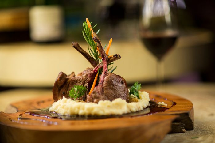 Garnished lamb chop on wooden serving plate with red pinot noir wine in background