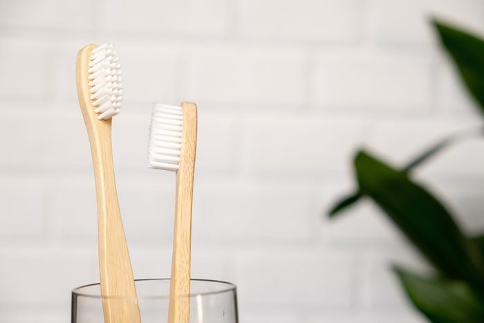 Close up of two bamboo toothbrushes and green leaf on a white background. Bathroom essentials. Dental care and zero waste concept.