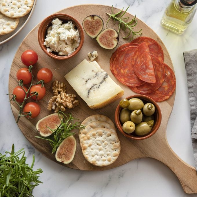 cheese board with figs, olives, meats, crackers, and tomatoes