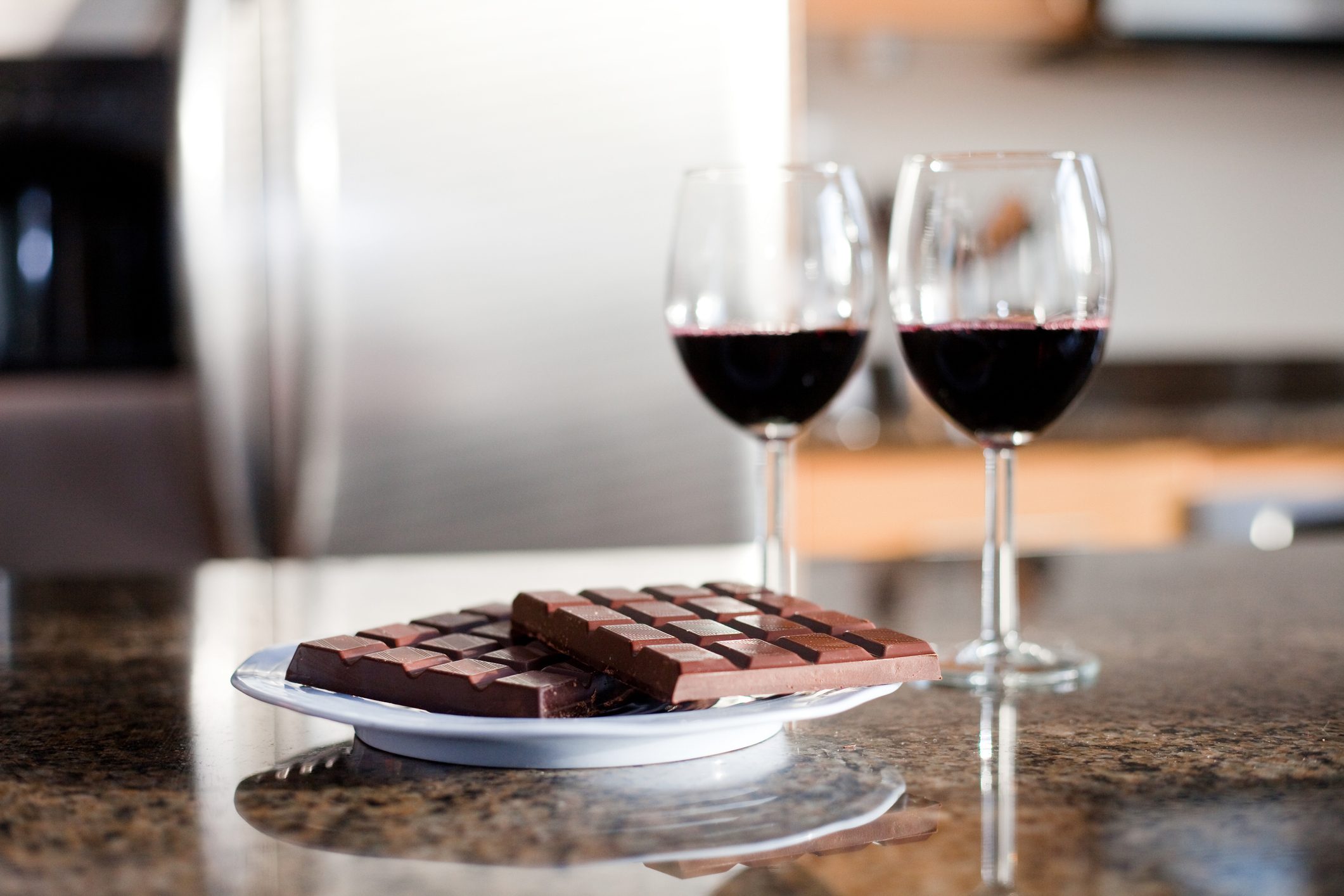 chocolate on a plate on kitchen counter with two glasses of red wine in the background