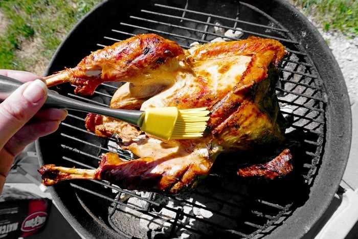 basting the turkey with a basting brush while it is still on the grill