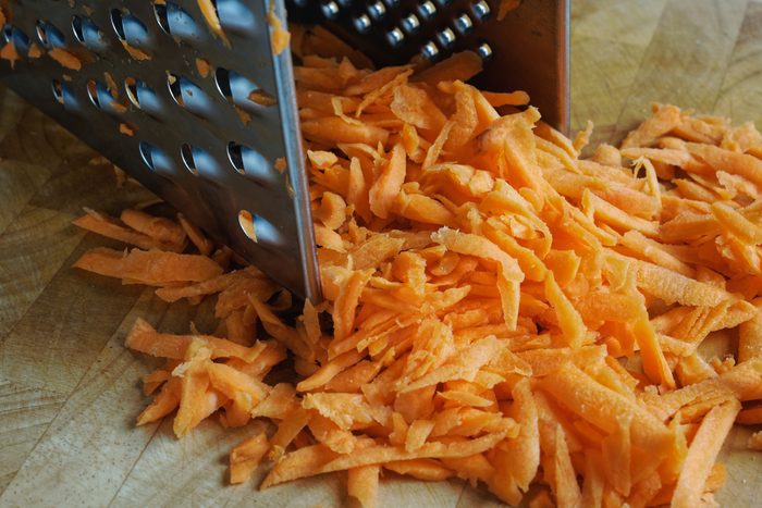 Grated carrots in a square grater on a wooden cutting board