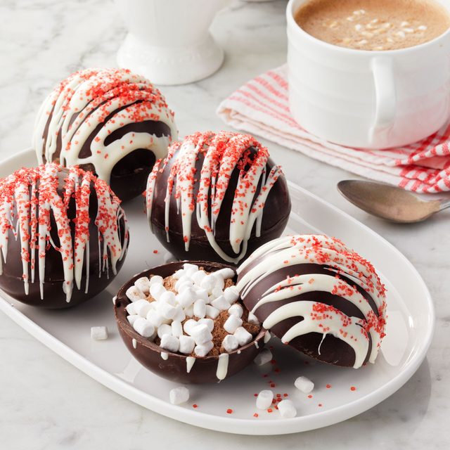 Hot Chocolate Bombs arranged on a white tray with a cup of hot cocoa in the background